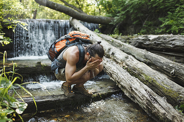 Junger Mann auf einer Wanderung erfrischend am Wasserfall