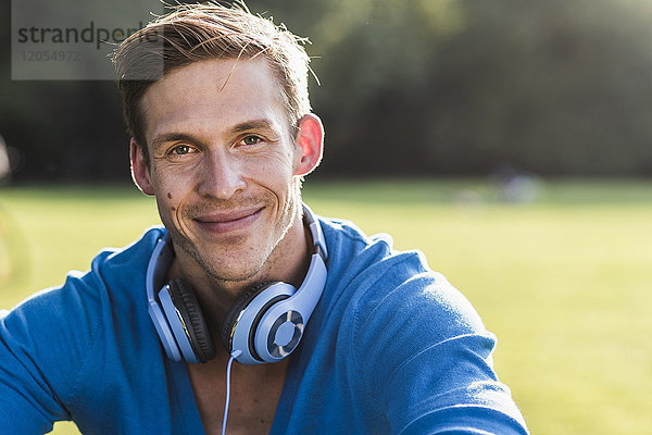 Porträt eines lächelnden Mannes mit Kopfhörer im Park