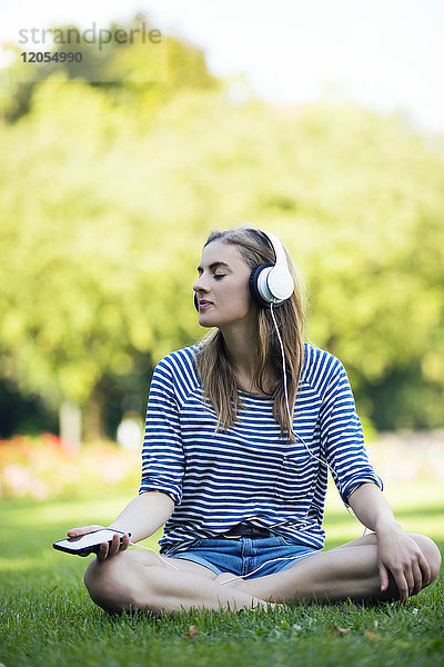 Junge Frau sitzt auf der Wiese und hört Musik mit Kopfhörern.