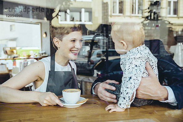 Kellnerin serviert Kaffee für lächelnde Kunden mit Baby im Cafe