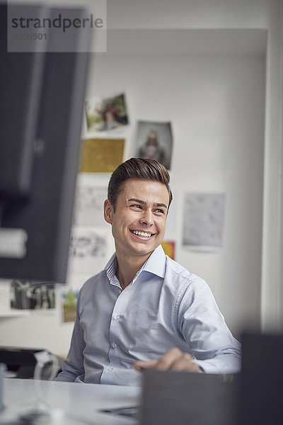 Porträt des lachenden jungen Geschäftsmannes am Schreibtisch im Büro