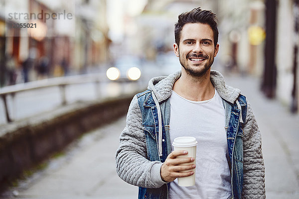 Porträt eines lächelnden Mannes mit Kaffee und Stadtstraße im Hintergrund
