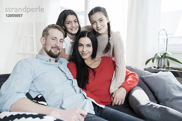 Familienporträt der Eltern und Zwillingstöchter auf Sofa im Wohnzimmer