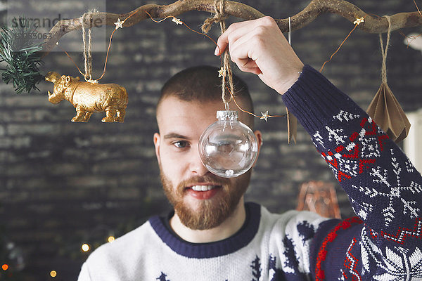 Porträt eines Mannes  der durch die transparente Weihnachtskugel schaut