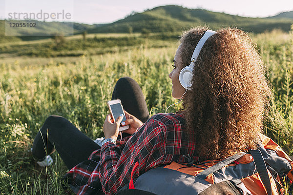 Teenagermädchen mit Rucksack Musik hören mit Kopfhörer auf einer Wiese