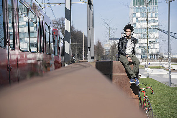 Lächelnder Mann sitzt an der Wand und hört Musik neben dem vorbeifahrenden Zug.