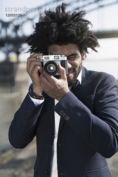 Mann im Anzug am Flussufer beim Fotografieren mit einer Vintage-Kamera