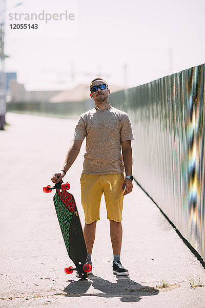 Portrait eines selbstbewussten jungen Mannes mit Longboard