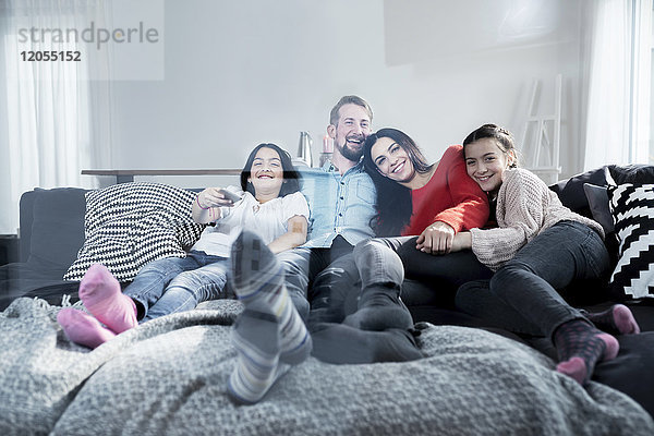 Glückliche Eltern und Zwillingstöchter auf dem Sofa im Wohnzimmer beim Fernsehen