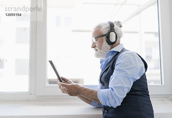 Erwachsener Mann mit Tablette und Kopfhörer am Fenster