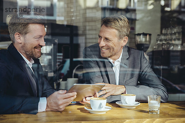 Zwei lächelnde Geschäftsleute mit Tablette in einem Cafe