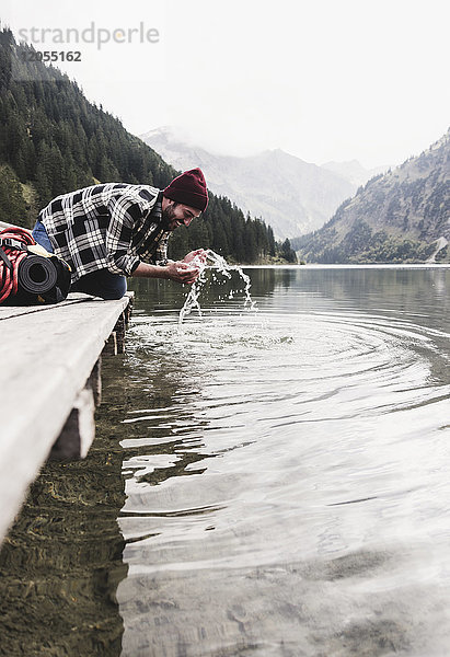 Österreich  Tirol  Alpen  Mann kniend am Steg erfrischend am Bergsee