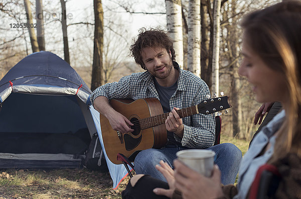Pärchen-Camping im Wald mit einem Mann  der Gitarre spielt.