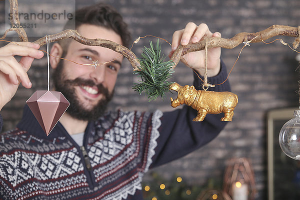 Lächelnder junger Mann  der zur Weihnachtszeit einen Zweig schmückt.
