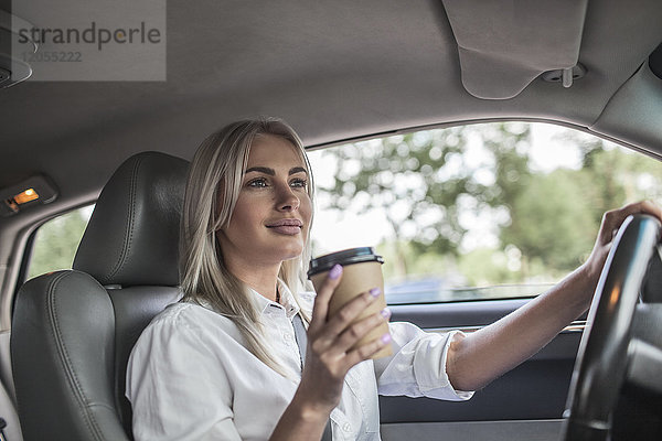 Lächelnde Geschäftsfrau hält Kaffee zum Mitnehmen und fährt Auto