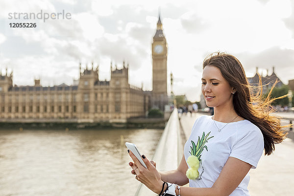 UK  London  Frau  die Nachrichten mit ihrem Smartphone auf der Westminster Bridge sendet.