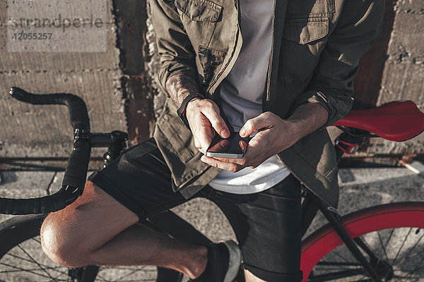 Junger Mann mit SMS auf dem Handy auf dem Fixie Bike