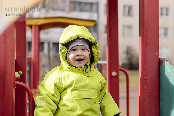 Portrait des glücklichen Kleinkindes mit Regenjacke auf dem Spielplatz