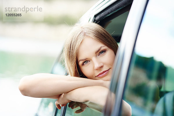 Porträt einer jungen Frau  die sich aus dem Autofenster lehnt.