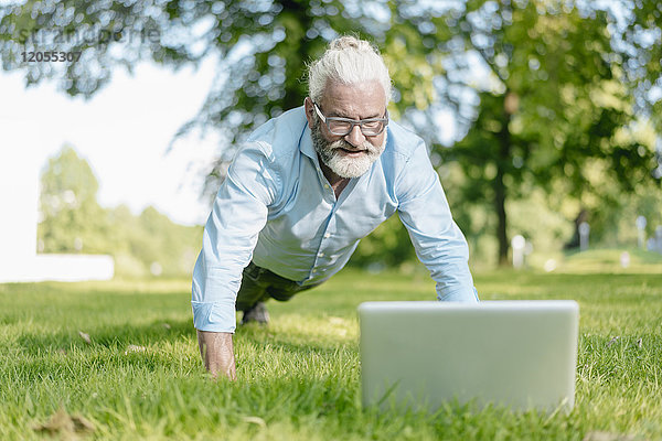 Erwachsener Mann mit Laptop-Training im Park