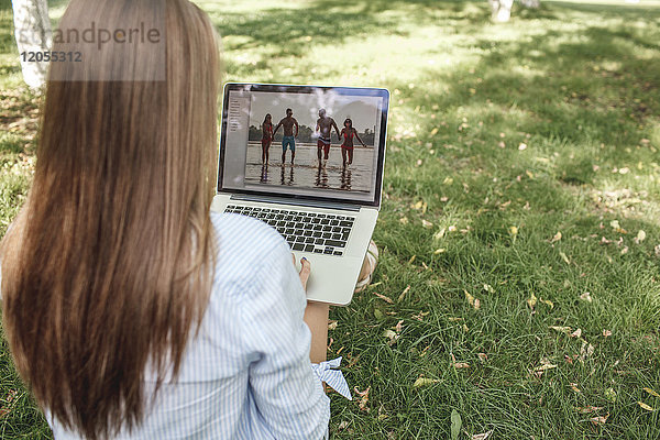 Junge Frau beim Betrachten der Fotografie auf dem Laptop-Bildschirm auf einer Wiese