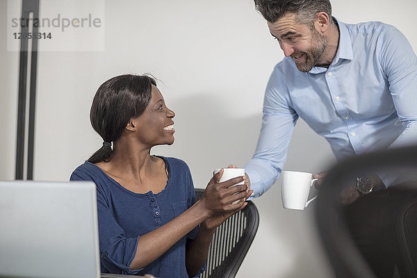 Lächelnde Kollegen mit Kaffeetassen im Büro im Gespräch