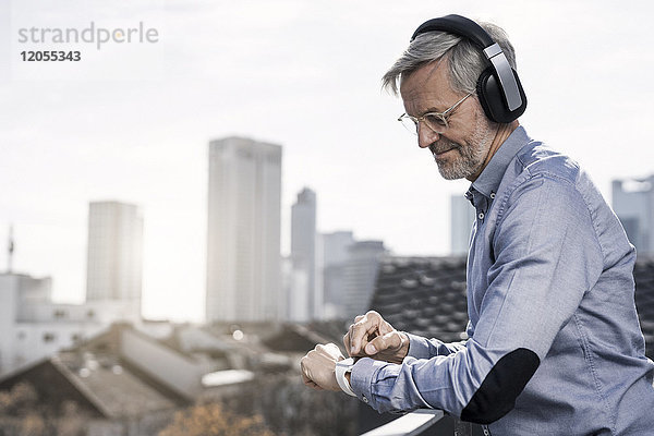 Grauhaariger Geschäftsmann mit Kopfhörern auf smartwatch