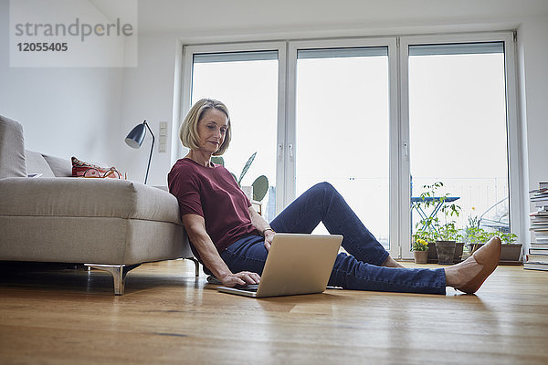 Reife Frau zu Hause mit Laptop auf dem Boden
