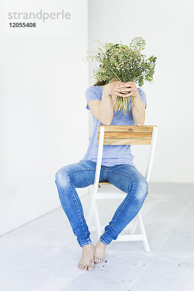 Frau sitzt auf einem Stuhl und hält Blumenstrauß vor ihrem Gesicht.