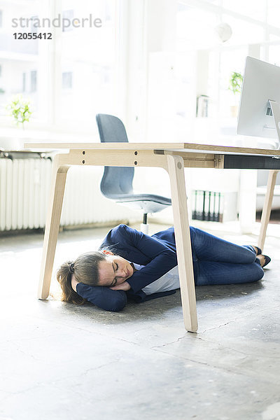 Geschäftsfrau unter dem Tisch liegend im Büro schlafend