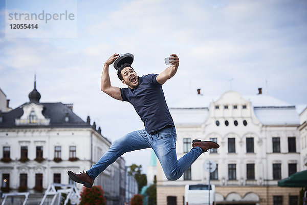 Mann springt und nimmt Selfie und hält Filzhut