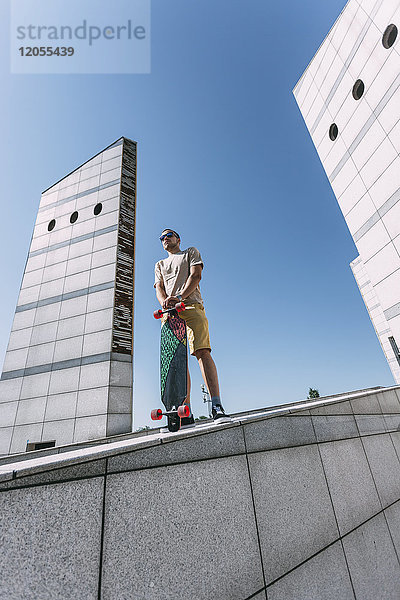 Junger Mann mit Longboard umgeben von moderner Architektur