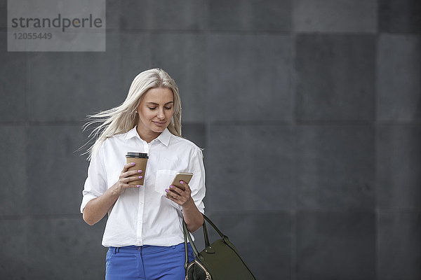 Lächelnde Geschäftsfrau mit Kaffee zum Mitnehmen und Handy unterwegs