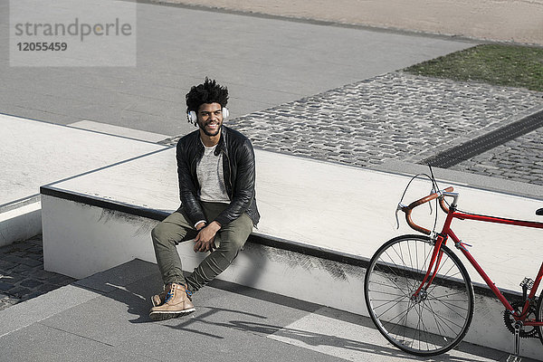 Lächelnder Mann  der Musik über Kopfhörer neben seinem Fahrrad hört.