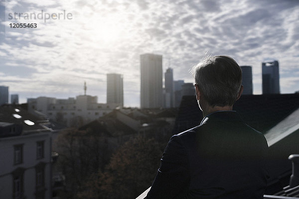 Grauhaariger Geschäftsmann auf dem Balkon mit Blick über die Stadt