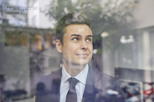 Porträt eines jungen Geschäftsmannes hinter Glasscheibe im Büro mit Blick nach oben