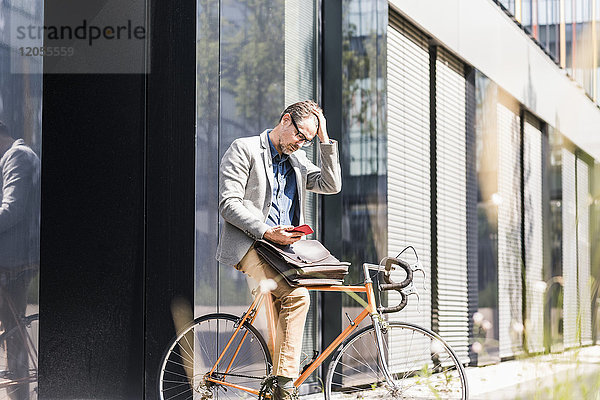 Schockierter Geschäftsmann auf dem Fahrrad beim Blick aufs Handy