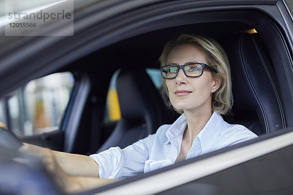 Blonde Geschäftsfrau mit Brille beim Autofahren