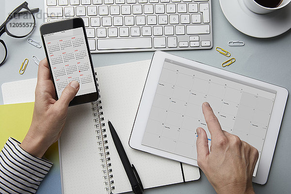 Draufsicht der Frau mit Smartphone und Tablett mit Kalender auf dem Schreibtisch