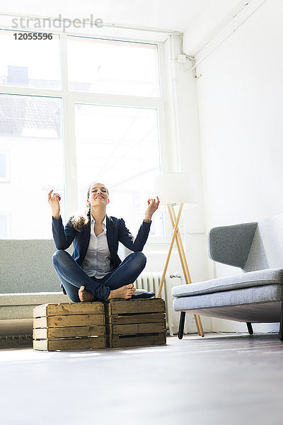Geschäftsfrau sitzt auf Kiste und praktiziert Yoga
