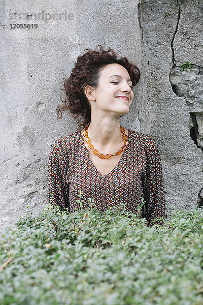 Lächelnde Frau in elegantem Kleid an der Wand lehnend