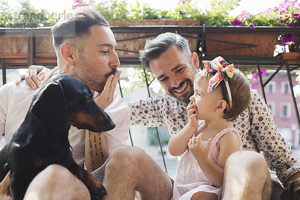 Glückliches schwules Paar mit Tochter und Hund auf dem Balkon