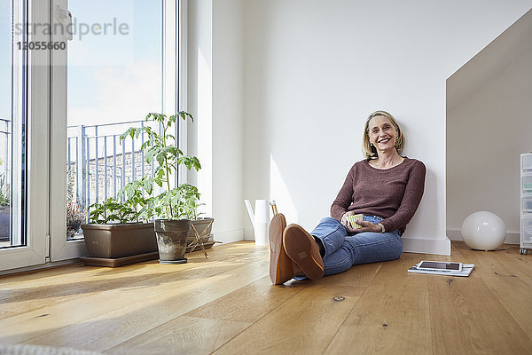 Porträt der lächelnden reifen Frau zu Hause auf dem Boden sitzend