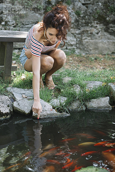 Frau hockt an einem Teich in einem Park