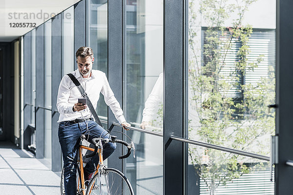 Geschäftsmann mit Handy auf dem Fahrrad im Bürogang