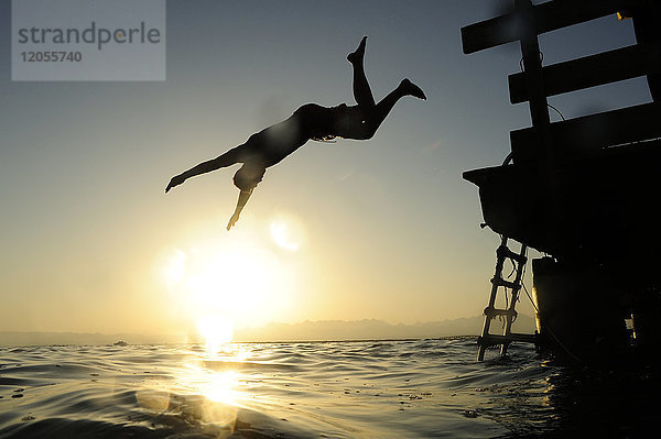 Mann  der bei Sonnenuntergang vom Steg ins Meer springt.