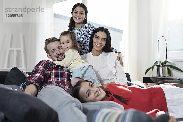 Porträt der Eltern und drei Töchter auf Sofa im Wohnzimmer