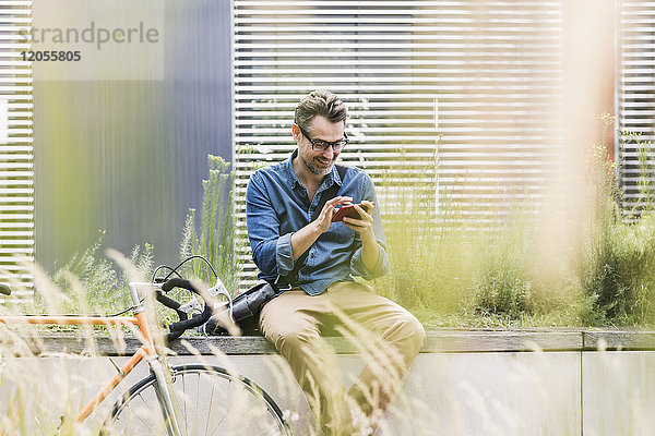 Lächelnder Geschäftsmann mit Handy neben dem Fahrrad