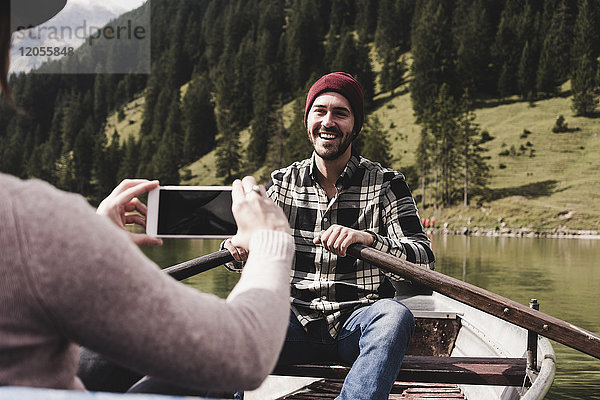 Österreich  Tirol  Alpen  Frau macht Handyfoto von lächelndem Mann im Ruderboot auf dem Bergsee