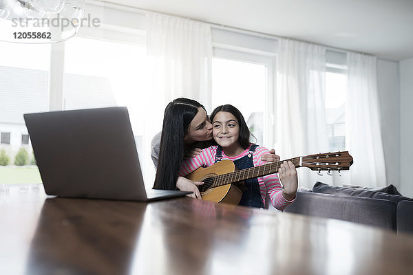 Mutter küsst Tochter beim Gitarrespielen vor dem Laptop